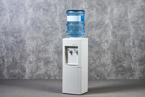 White water cooler gallon in office against gray textured wall background. International Exhibition furniture elements in large warehouse interior.