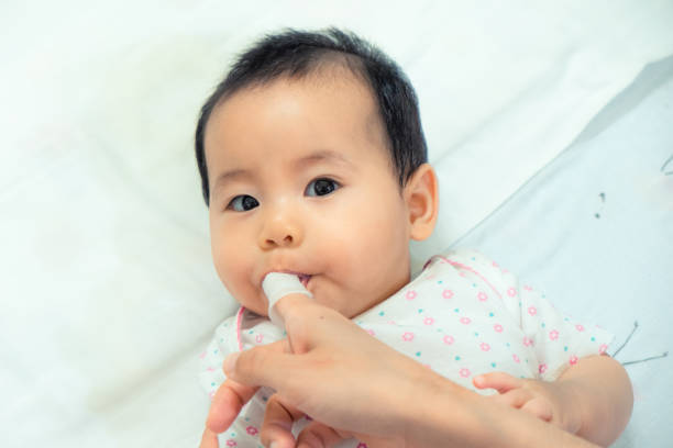 matka używa palca do czyszczenia azjatyckiego języka dziecka czystą gazą. - finger in mouth obrazy zdjęcia i obrazy z banku zdjęć