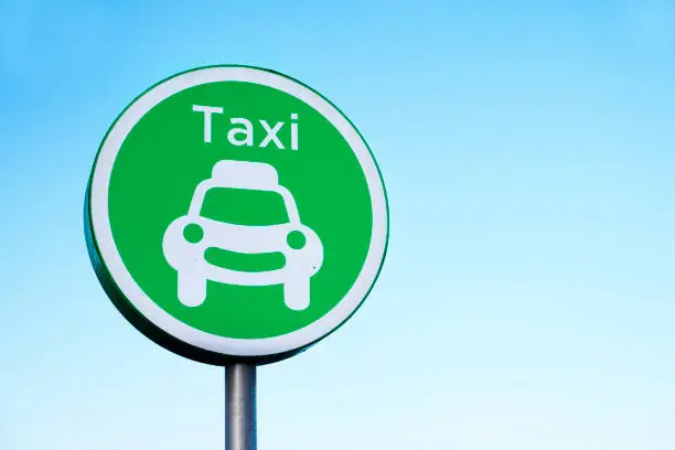 Taxi rank sign and vehicle car symbol against plain blue sky for private transport uk