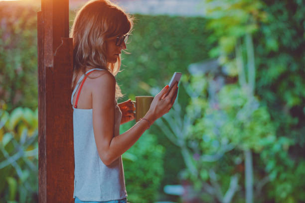 istock Young woman using cellphone and drinking coffee / tea on a porch. 1051648610