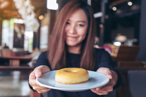 A beautiful asian woman holding and showing a plate of donut with feeling happy and good lifestyle in the modern cafe
