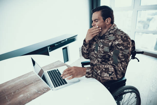 istock Yawning Military Man in Wheelchair Work on Laptop 1051655890