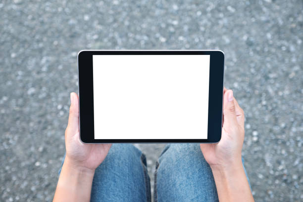 istock Top view mockup image of a woman holding black tablet pc with blank white screen while sitting on the street background 1051659036