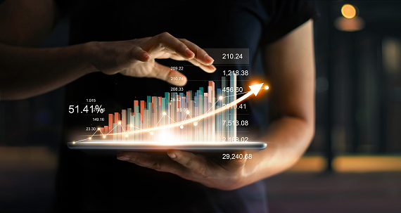 Empresario sosteniendo tablet y muestra un holograma virtual creciente de estadísticas, gráfico y tabla con flechas sobre fondo oscuro. Mercado de valores. Concepto de crecimiento, planeación y estrategia de negocio. photo