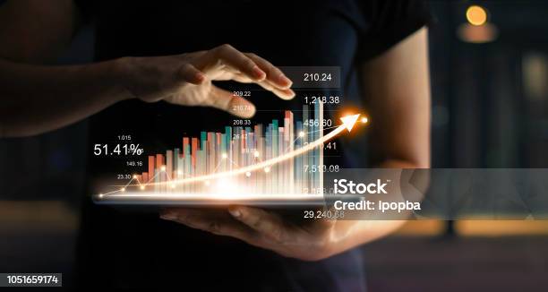 Businessman Holding Tablet And Showing A Growing Virtual Hologram Of Statistics Graph And Chart With Arrow Up On Dark Background Stock Market Business Growth Planing And Strategy Concept Stock Photo - Download Image Now