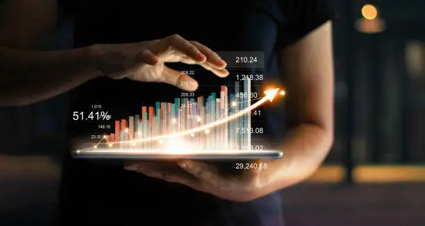 Photo of Businessman holding tablet and showing a growing virtual hologram of statistics, graph and chart with arrow up on dark background. Stock market. Business growth, planing and strategy concept.