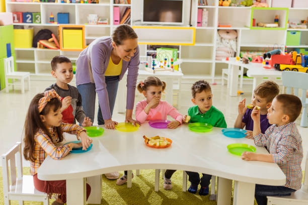 szczęśliwy nauczyciel z grupą dzieci na przerwie obiadowej w przedszkolu. - apple eating healthy eating friendship zdjęcia i obrazy z banku zdjęć