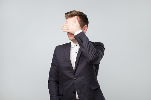 Caucasian man in suit covering his eyes He does not want to look on what is going on. It is not my business, not my problem
