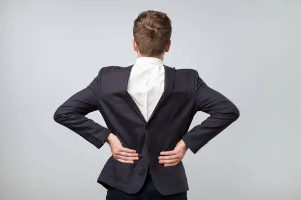Studio shot of a mature caucasian man wearing his suit on backwards, gray background. He lost his mind from continuous work. Obvious mental problems