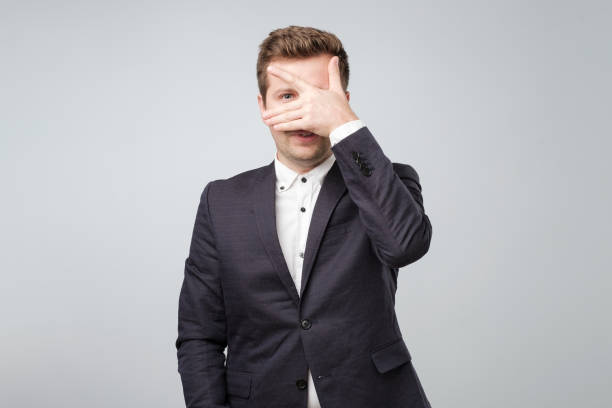 shocked attractive nice handsome young man in suit closing his eyes with palm and peeping trying to see someone secret - hiding humor occupation office imagens e fotografias de stock
