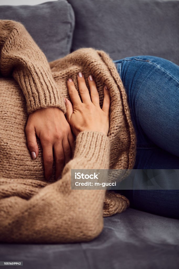 Woman having stomach issues / problems while lying on the couch. Stomachache Stock Photo