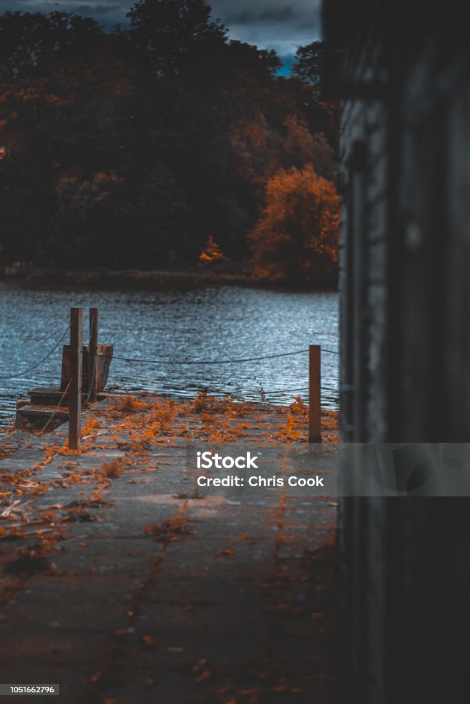 A shed on a lake A cold blue lake in the middle of Autumn surrounded by trees with orange leaves, paving and a shed. Autumn Stock Photo