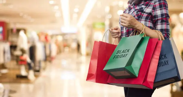 Photo of Black Friday, Woman holding many shopping bags while walking in the shopping mall background.