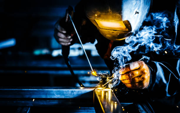 saldatore protetto da maschere professionali che lavora sulla saldatura dei metalli e scintille metalliche. - factory building flash foto e immagini stock