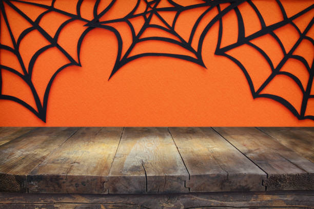 istock Halloween holiday concept. Empty rustic table in front of Spider webs over orange background. Ready for product display montage. 1051674160