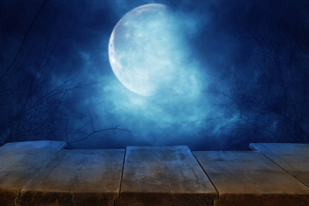 istock Halloween holiday concept. Empty rustic table in front of scary and misty night sky and full moon background. Ready for product display montage. 1051674198