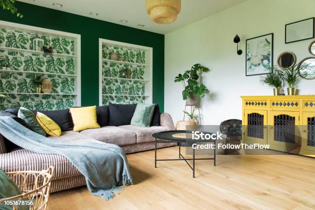 Stylish And Modern Interior With Sofa Colors Pillows Flowers And Wooden Floor Sunny And Bright Living Room Stock Photo - Download Image Now