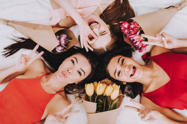 Top View Three Girls Lying on Bed with Flowers.