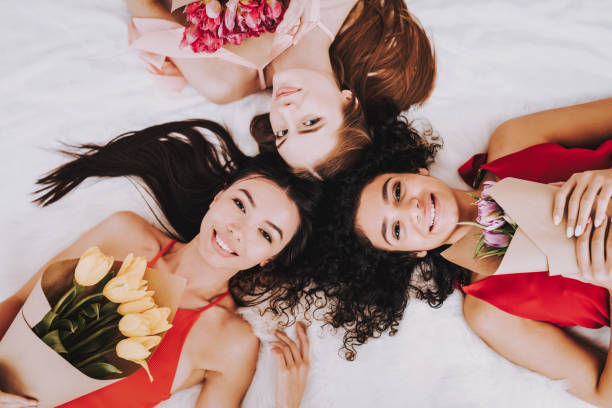 istock Three Happy Girls Lying on White Bed with Flowers. 1051678596