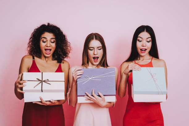 Surprised Girls Open and Look on Three Gift Boxes. Pink and Red Dresses. Pink Background. Celebrating Women's Day. Emotional Women. Happy Woman. Gift Box. Gife Bag. Girls Look in Gift Box. Beautiful Woman. Womans Emotion. Girls Open Gift Boxes. bachelor and bachelorette parties stock pictures, royalty-free photos & images