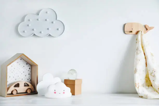 Photo of The modern sandinavian newborn baby room with mock up poster frame, wooden car, boxes and clouds. Minimalistic and cozy interior with white walls.