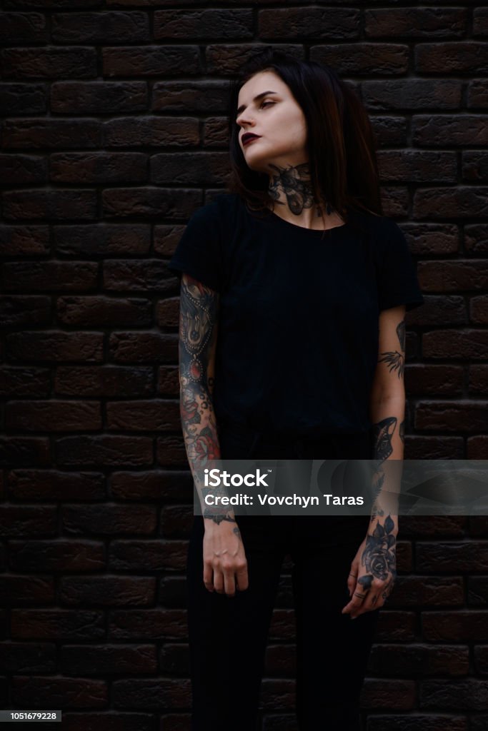 Beautiful Slim Brunette Girl With Black Lips Tattoos And Piercing Wearing  Black Clothes Standing Over Brick Wall Stock Photo - Download Image Now -  iStock