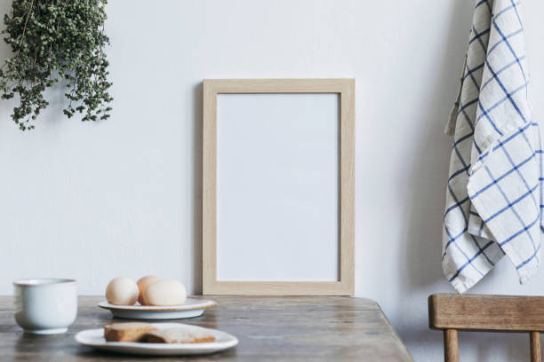 istock Stylish interior design of kitchen space with small table with mock up frame, herbs, cups of tea and eggs. Minimalistic interior. 1051680038