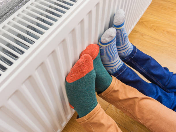 donna e bambino che indossano un paio colorato di calze lanose che riscaldano i piedi freddi davanti al radiatore di riscaldamento in inverno. riscaldatore elettrico o a gas a casa. - electric heater foto e immagini stock