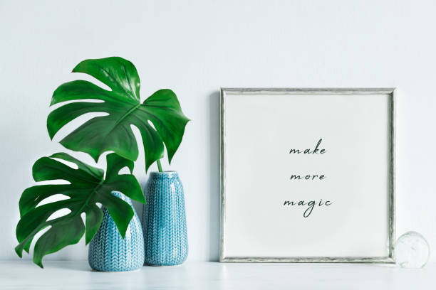 istock Modern and minimalistic composition of mock up photo frame with green tropical leafs in design vase. Stylish concept of mockup frame. White backgrounds wall. 1051686764