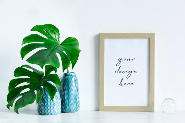 istock Modern and minimalistic composition of mock up photo frame with green tropical leafs in design vase. Stylish concept of mockup frame. White backgrounds wall. 1051686808