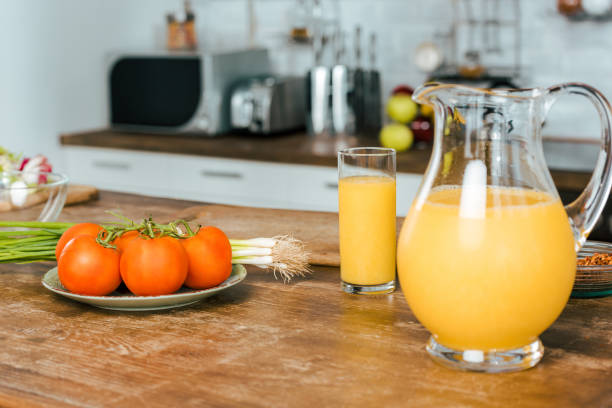 close-up foto de tomates crudos con puerro y jarra de jugo de naranja sobre la mesa en la cocina - healthy eating food and drink raw leek fotografías e imágenes de stock