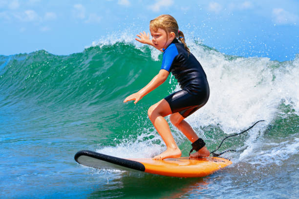 Young surfer rides on surfboard with fun on sea waves Happy baby girl - young surfer ride on surfboard with fun on sea waves. Active family lifestyle, kids outdoor water sport lessons and swimming activity in surf camp. Summer vacation with child. raro stock pictures, royalty-free photos & images