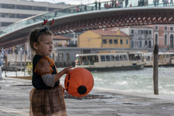 Cute little dressed up for Halloween having a toy pumpkin in her hands, near by piazzale Roma in Venice Italy