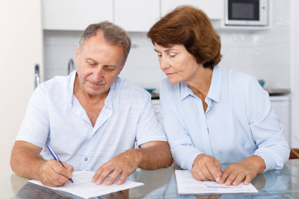 istock Smiling mature couple  at table in home kitchen filling up documents 1051695586