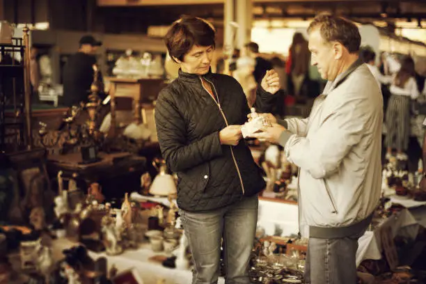 happy man and his wife are visiting market of old things and looking collectible outdoors.