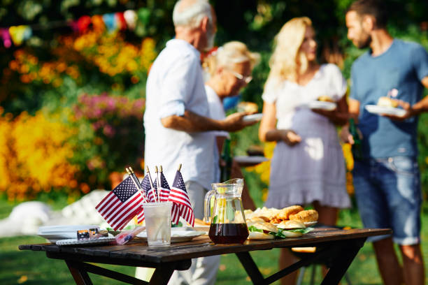 Multi-generation Family Celebrating 4th of July Multi-generation family on picnic in back yard celebrating 4th of July - Independence Day. Selective focus on food and drink with american flags on the table. independence day holiday stock pictures, royalty-free photos & images