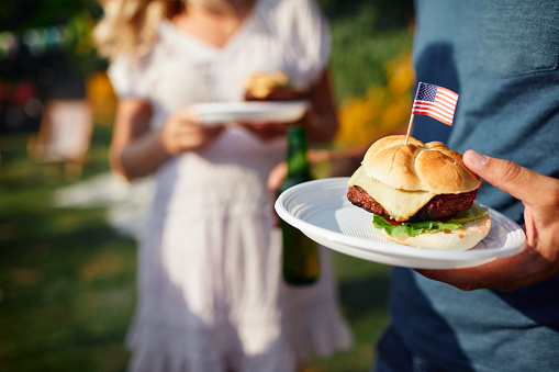 Family on picnic in back yard celebrating 4th of July - Independence Day. Focus on burger with USA flag.