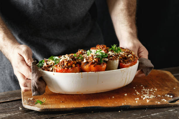 Male hands holding cooked stuffed peppers Male hands holding cooked stuffed peppers with green lentils, corn, salsa and almonds in baking dish on wooden table copy space. Healthy, vegetarian food concept hungarian pepper stock pictures, royalty-free photos & images