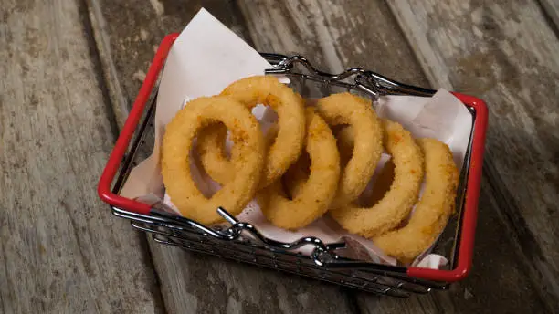 Fried onion rings in basket on aged background