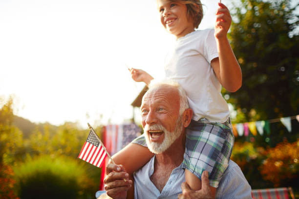 Multi-generation Family Celebrating 4th of July Multi-generation family on picnic in back yard celebrating 4th of July - Independence Day. Grandfather carrying grandson on shoulders. picnic photos stock pictures, royalty-free photos & images