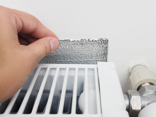 istock Hand holding energy-efficient thermal insulation on the wall behind the heating radiator. 1051709460