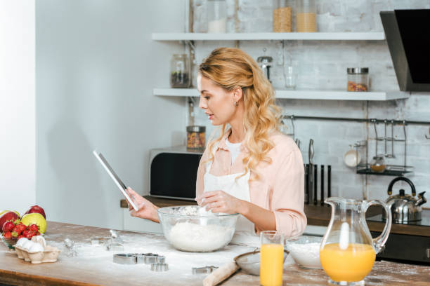 istock beautiful young woman making dough and using tablet at kitchen 1051709842