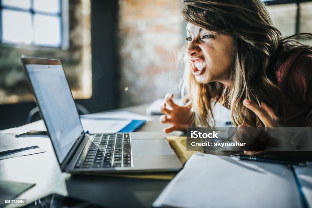 Frustrated woman received a problematic e-mail over computer. Angry freelance worker feeling displeased after reading an e-mail on a computer. Anger Stock Photo