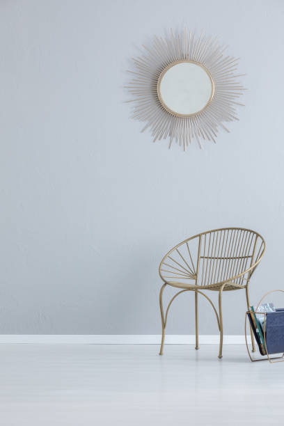 istock Gold mirror on grey empty wall above armchair in simple hall interior with copy space. Real photo 1051720180