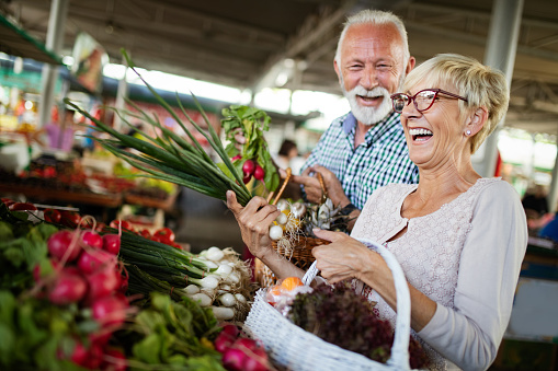Sonriente pareja senior con cesta con verduras en el mercado photo