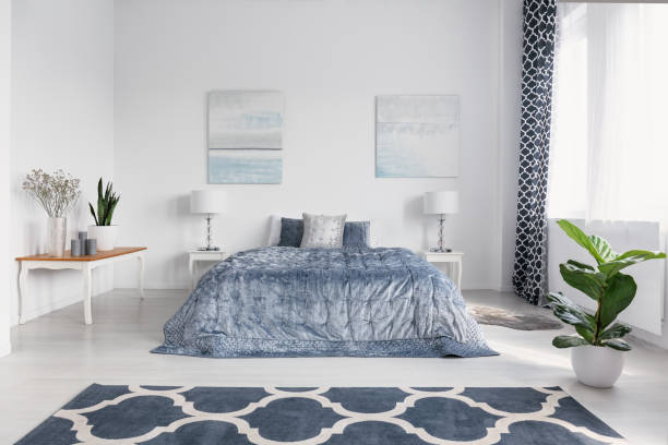 istock Elegant bedroom interior with big comfortable bed with blue bedding, paintings on the wall and patterned carpet on the floor, real photo 1051724890
