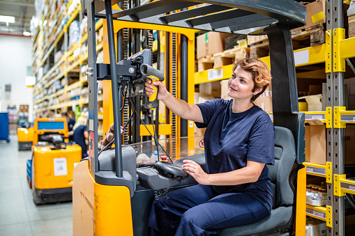 Woman scanning product with bar code reader in warehouse while sitting in forklift