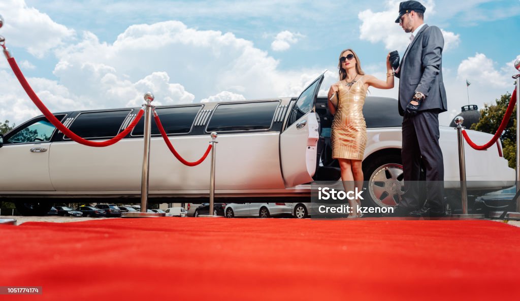 Driver helping VIP woman or star out of limo on red carpet Driver helping VIP woman or star out of limo on red carpet to a reception Red Carpet Event Stock Photo