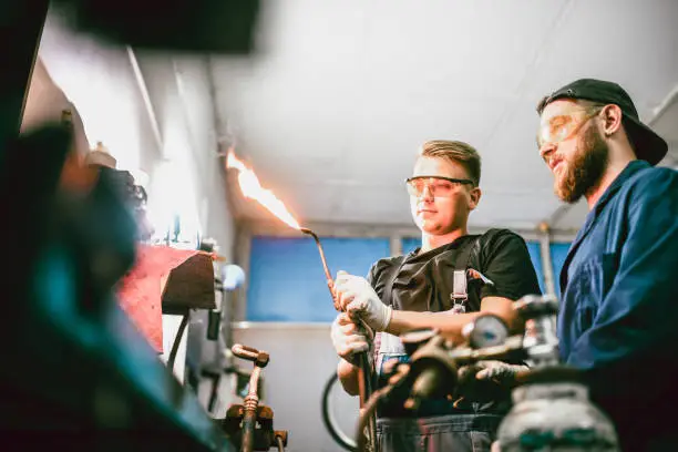 Mechanic And Apprentice Working On Fixing Tool With Blowtorch