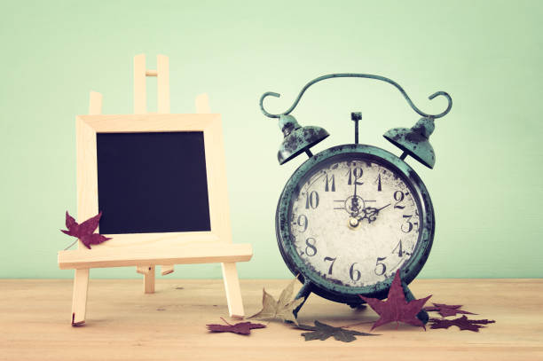 istock Image of autumn Time Change. Fall back concept. Dry leaves and vintage alarm Clock on rustic wooden table. 1051789328